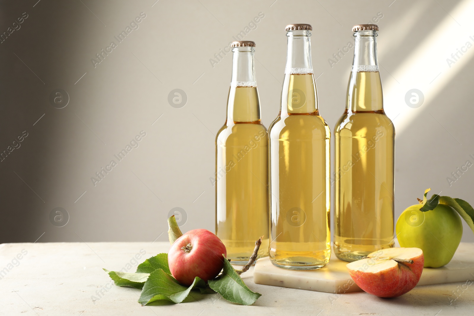 Delicious cider in glass bottles and apples on gray table against light background. Space for text Photo of Delicious cider in glass bottles and apples on gray table against light background. Space for text