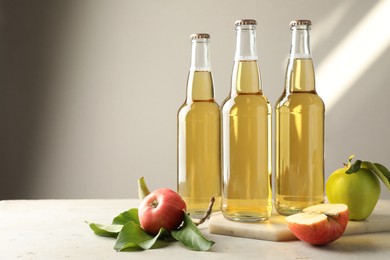 Photo of Delicious cider in glass bottles and apples on gray table against light background. Space for text