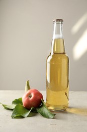 Photo of Delicious cider in glass bottle and apples on gray table against light background