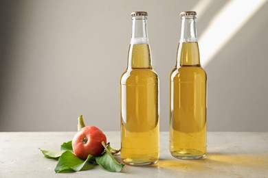 Photo of Delicious cider in glass bottles and apples on gray table against light background