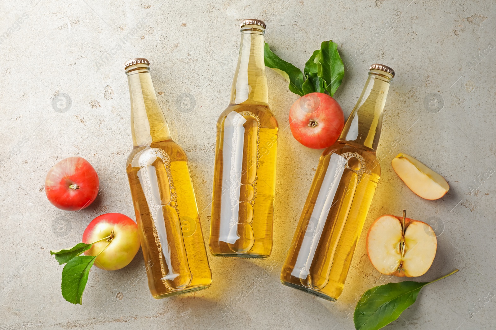Photo of Delicious cider in glass bottles and apples on gray textured table, flat lay