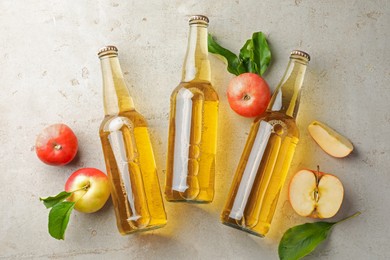 Photo of Delicious cider in glass bottles and apples on gray textured table, flat lay