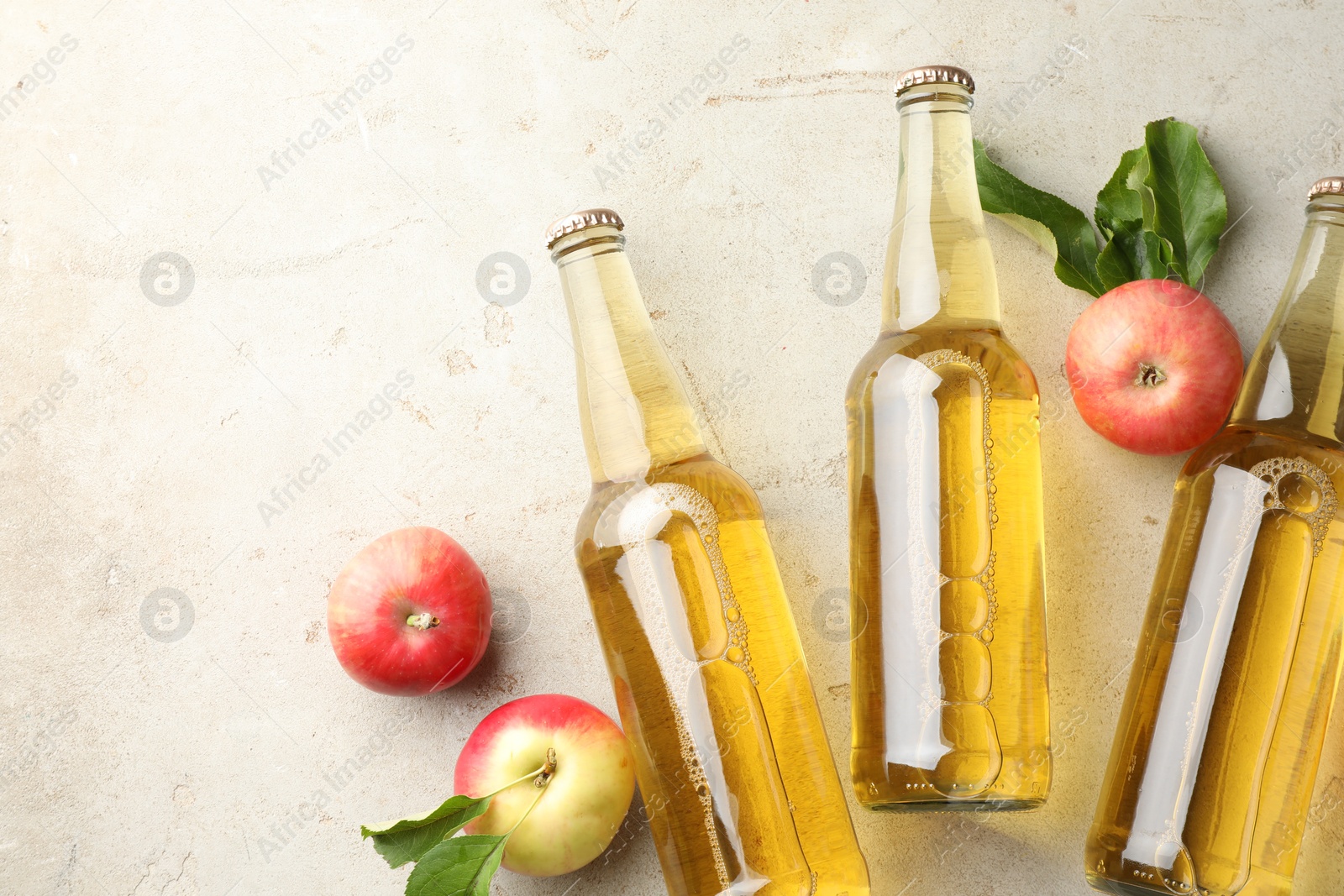 Delicious cider in glass bottles and apples on gray textured table, flat lay. Space for text Photo of Delicious cider in glass bottles and apples on gray textured table, flat lay. Space for text
