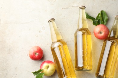 Photo of Delicious cider in glass bottles and apples on gray textured table, flat lay. Space for text