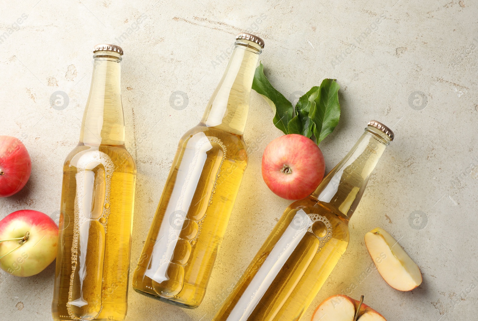 Delicious cider in glass bottles and apples on gray textured table, flat lay Photo of Delicious cider in glass bottles and apples on gray textured table, flat lay