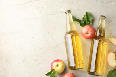 Photo of Delicious cider in glass bottles and apples on gray textured table, flat lay. Space for text
