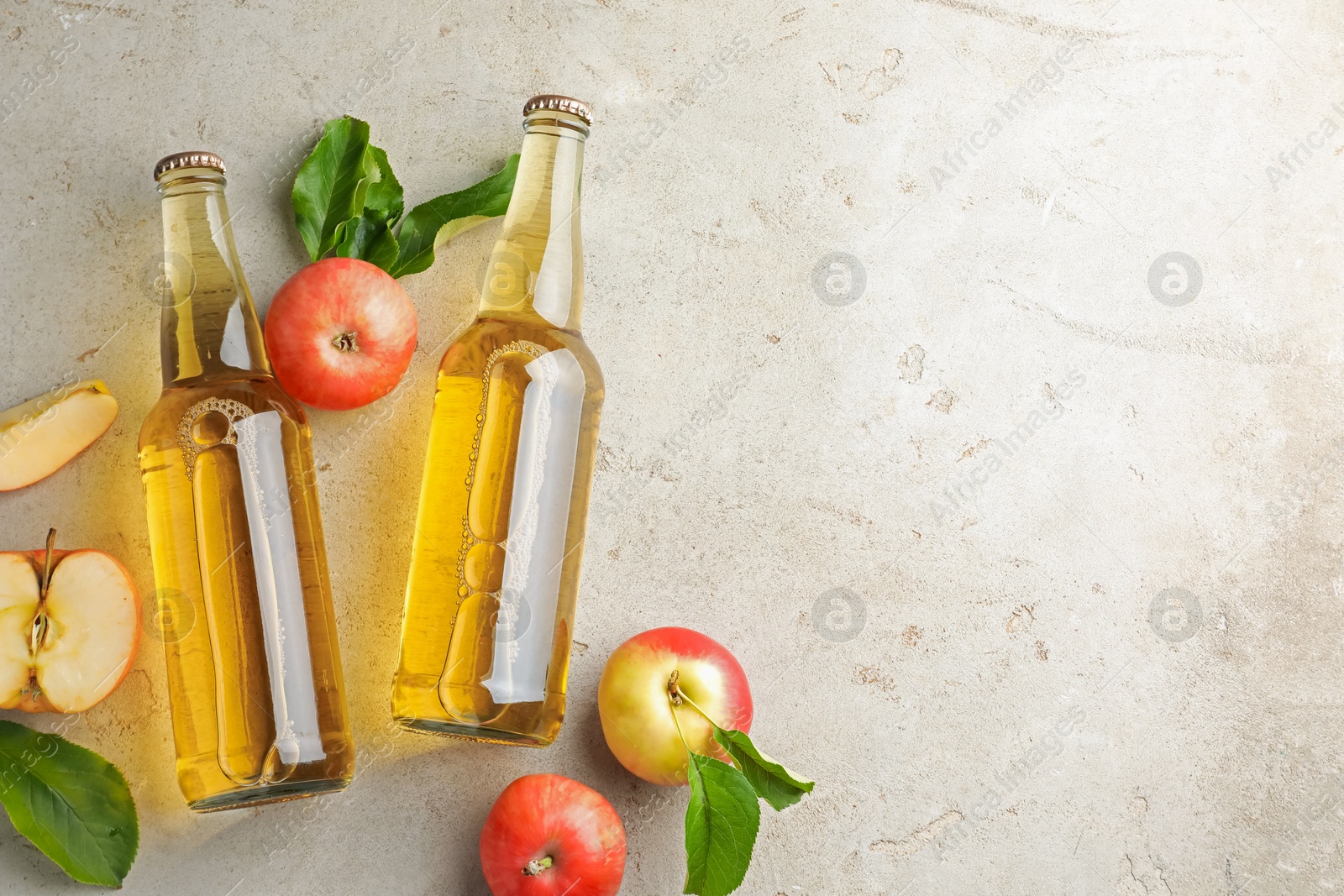 Photo of Delicious cider in glass bottles and apples on gray textured table, flat lay. Space for text