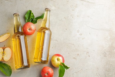 Photo of Delicious cider in glass bottles and apples on gray textured table, flat lay. Space for text
