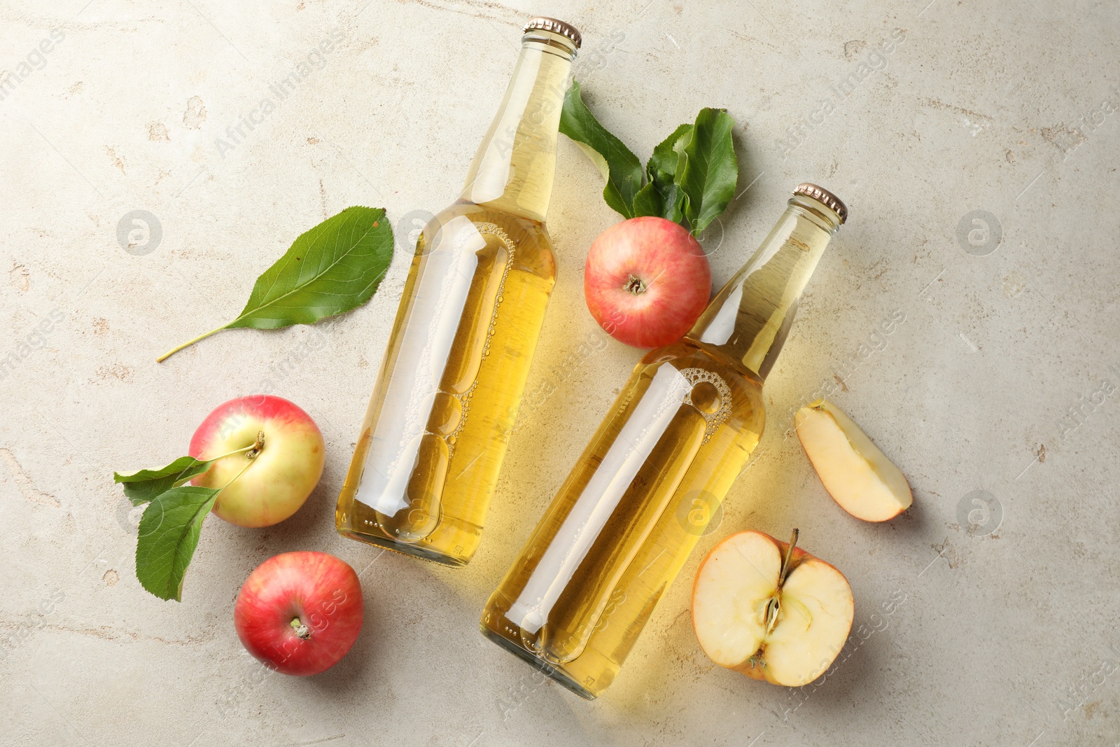 Photo of Delicious cider in glass bottles and apples on gray textured table, flat lay
