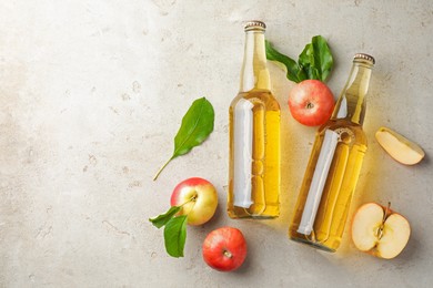 Photo of Delicious cider in glass bottles and apples on gray textured table, flat lay. Space for text