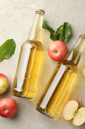 Photo of Delicious cider in glass bottles and apples on gray textured table, flat lay