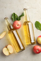 Photo of Delicious cider in glass bottles and apples on gray textured table, flat lay