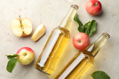 Photo of Delicious cider in glass bottles and apples on gray textured table, flat lay