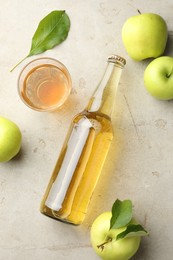 Photo of Delicious cider in bottle, glass and apples with green leaves on gray textured table, flat lay