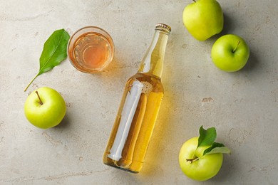 Photo of Delicious cider in bottle, glass and apples with green leaves on gray textured table, flat lay