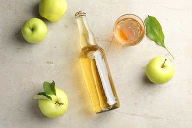 Photo of Delicious cider in bottle, glass and apples with green leaves on gray textured table, flat lay