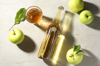 Photo of Delicious cider in bottle, glass and apples with green leaves on gray textured table, flat lay