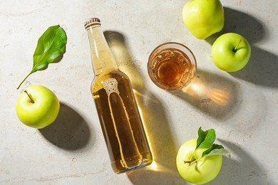 Photo of Delicious cider in bottle, glass and apples with green leaves on gray textured table, flat lay