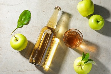 Photo of Delicious cider in bottle, glass and apples with green leaves on gray textured table, flat lay