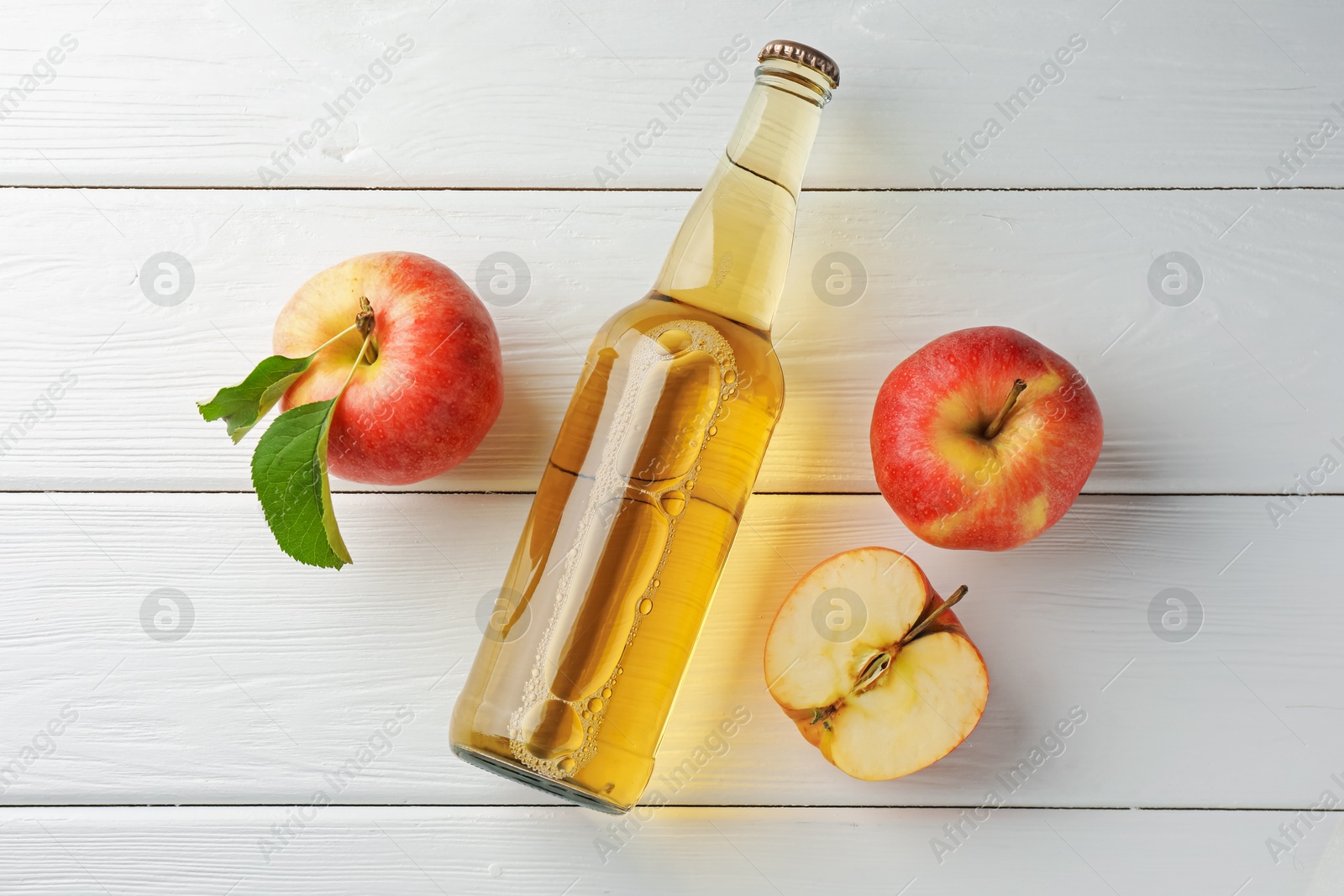 Photo of Delicious cider in glass bottle and apples on white wooden table, flat lay