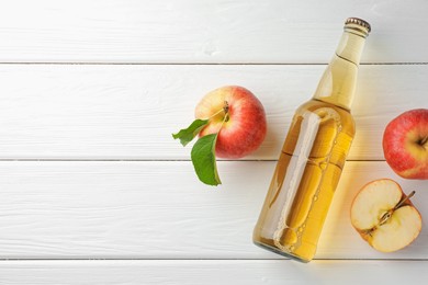 Photo of Delicious cider in glass bottle and apples on white wooden table, flat lay. Space for text