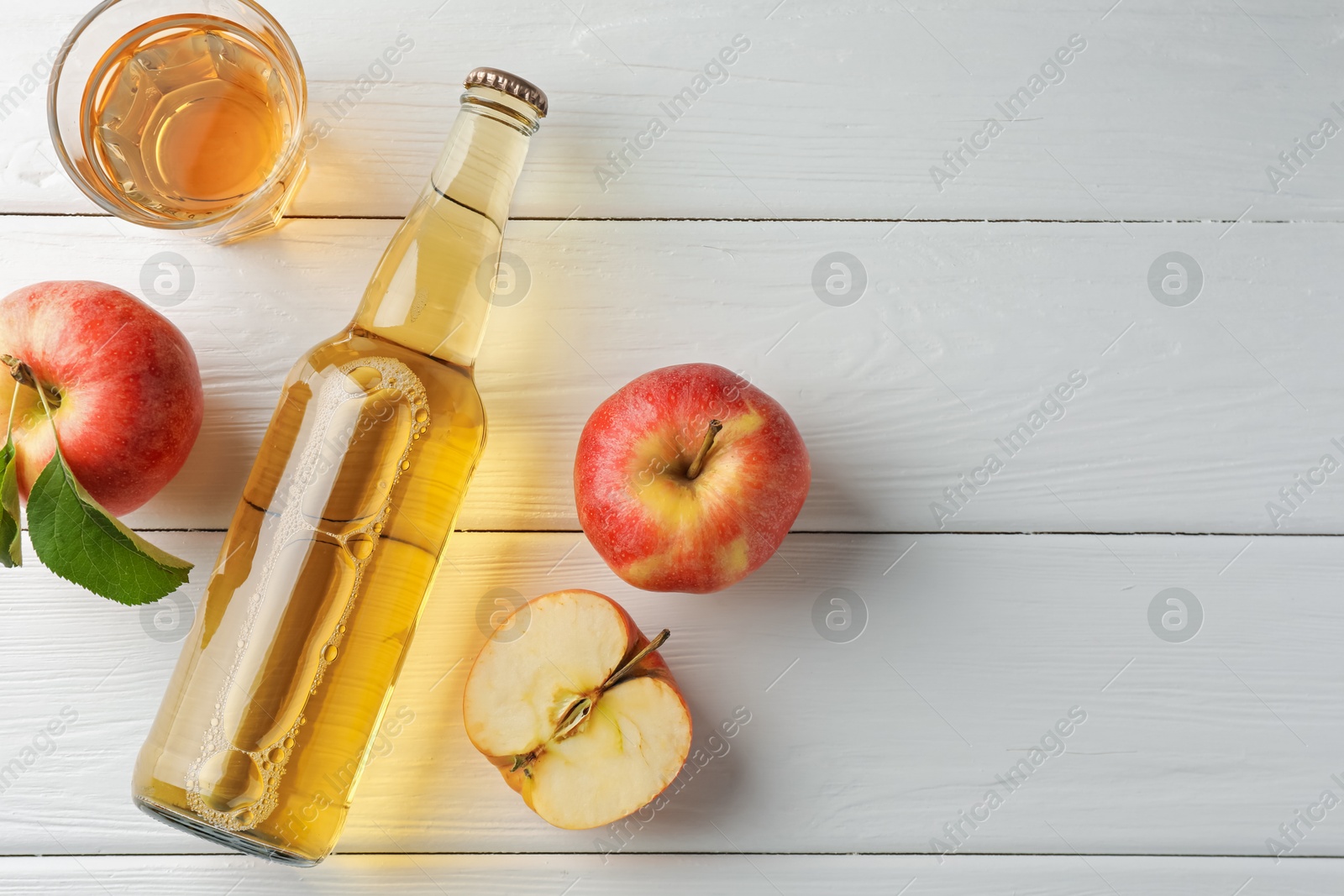 Photo of Delicious cider in glass bottle and apples on white wooden table, flat lay. Space for text