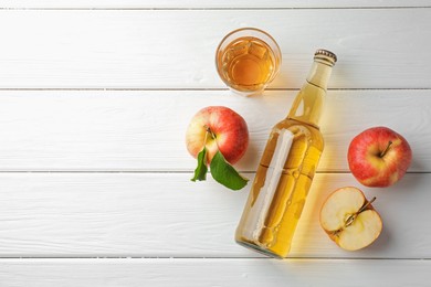 Photo of Delicious cider in glass bottle and apples on white wooden table, flat lay. Space for text