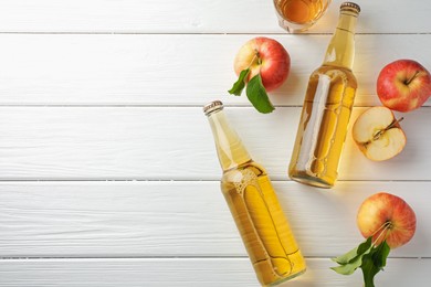 Photo of Delicious cider in glass bottles and apples on white wooden table, flat lay. Space for text