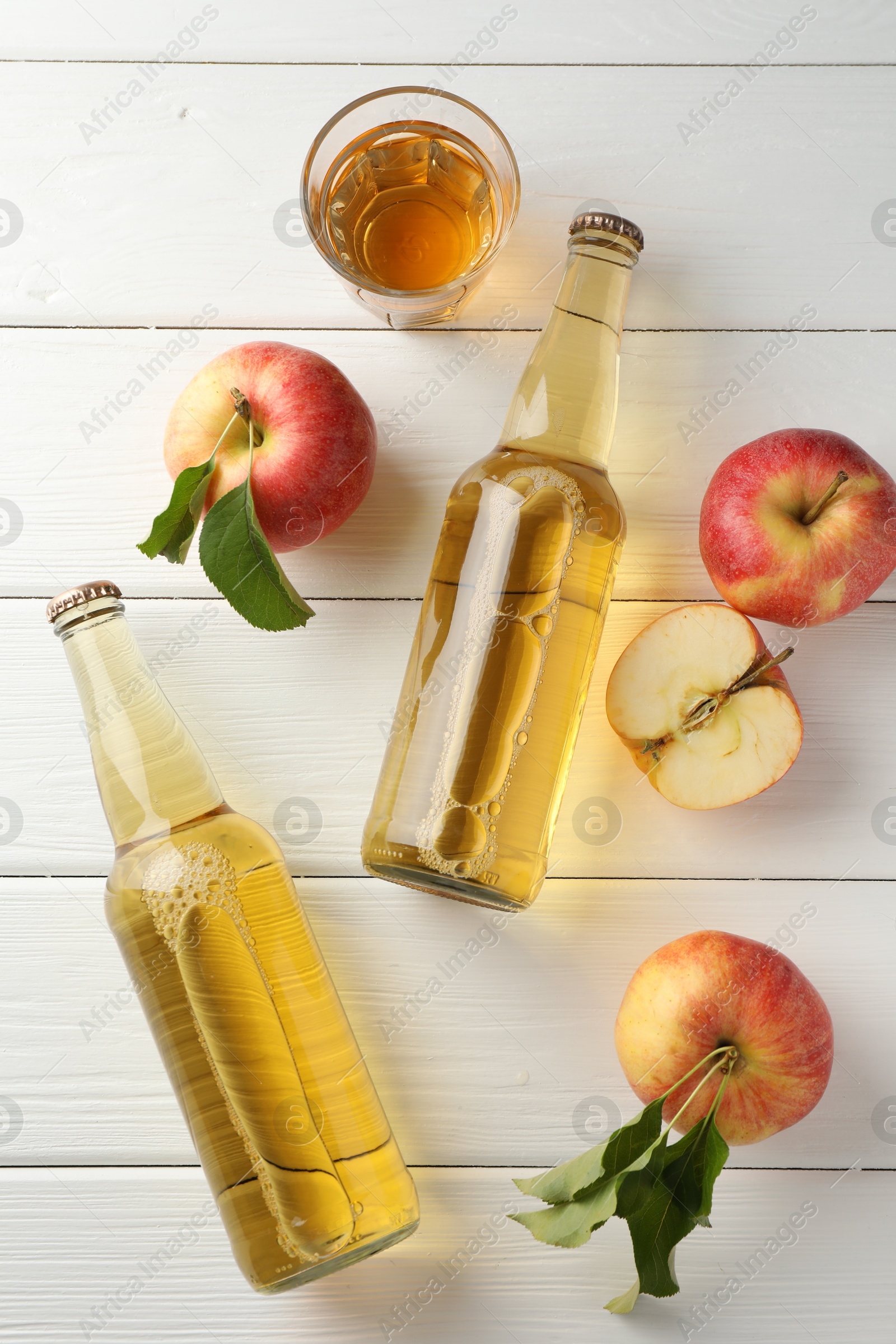 Photo of Delicious cider in glass bottles and apples on white wooden table, flat lay