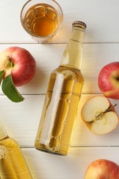 Photo of Delicious cider in glass bottles and apples on white wooden table, flat lay