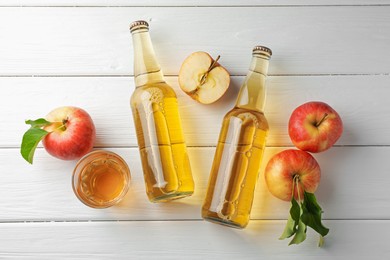 Photo of Delicious cider in glass bottles and apples on white wooden table, flat lay