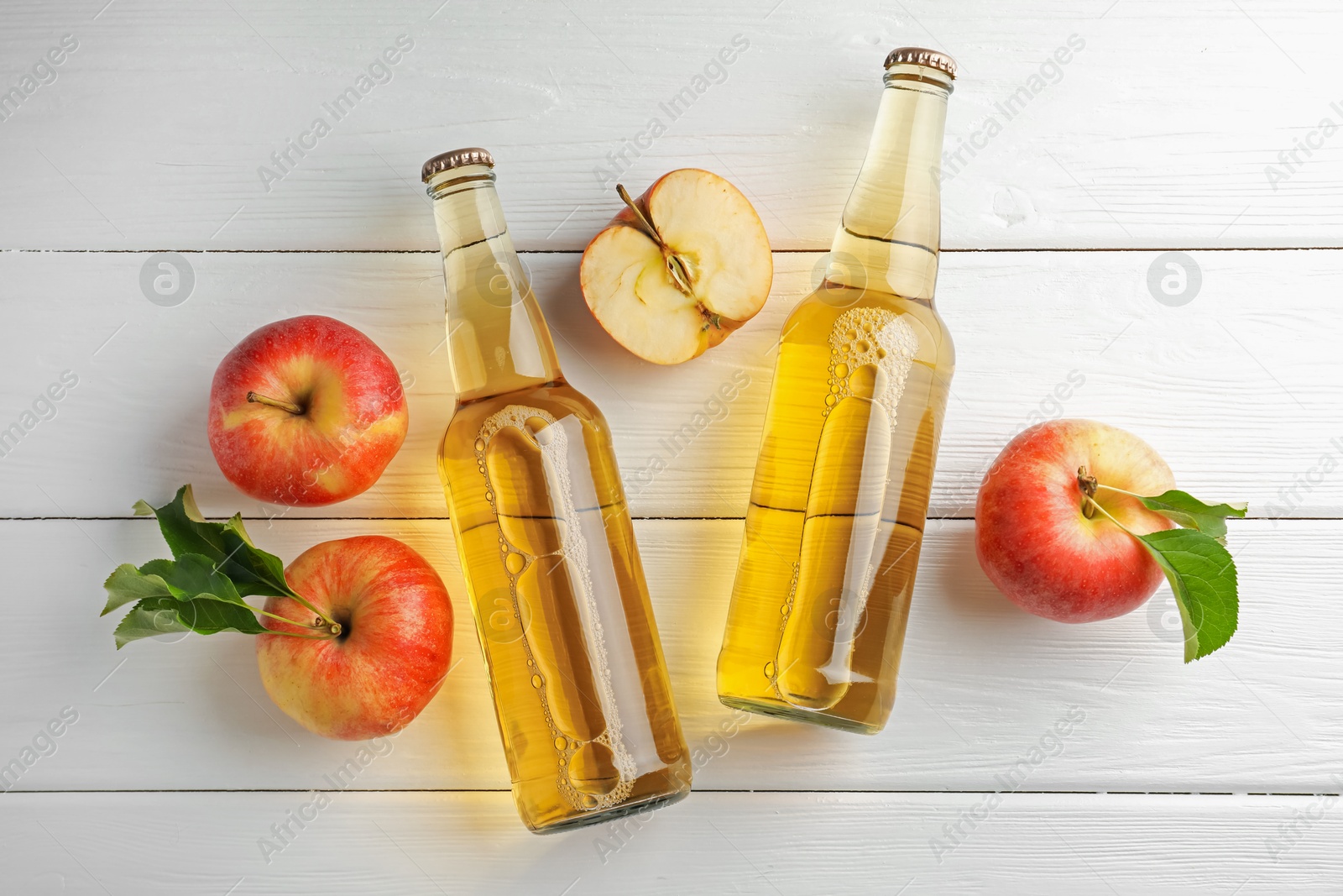 Photo of Delicious cider in glass bottles and apples on white wooden table, flat lay