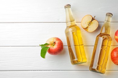 Photo of Delicious cider in glass bottles and apples on white wooden table, flat lay. Space for text