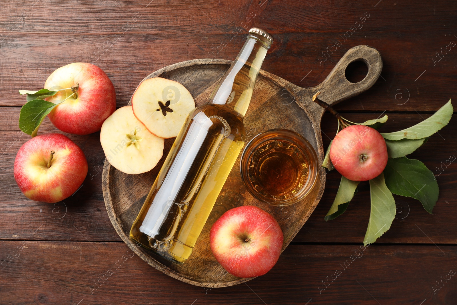 Photo of Delicious cider in bottle, glass and apples with green leaves on wooden table, flat lay