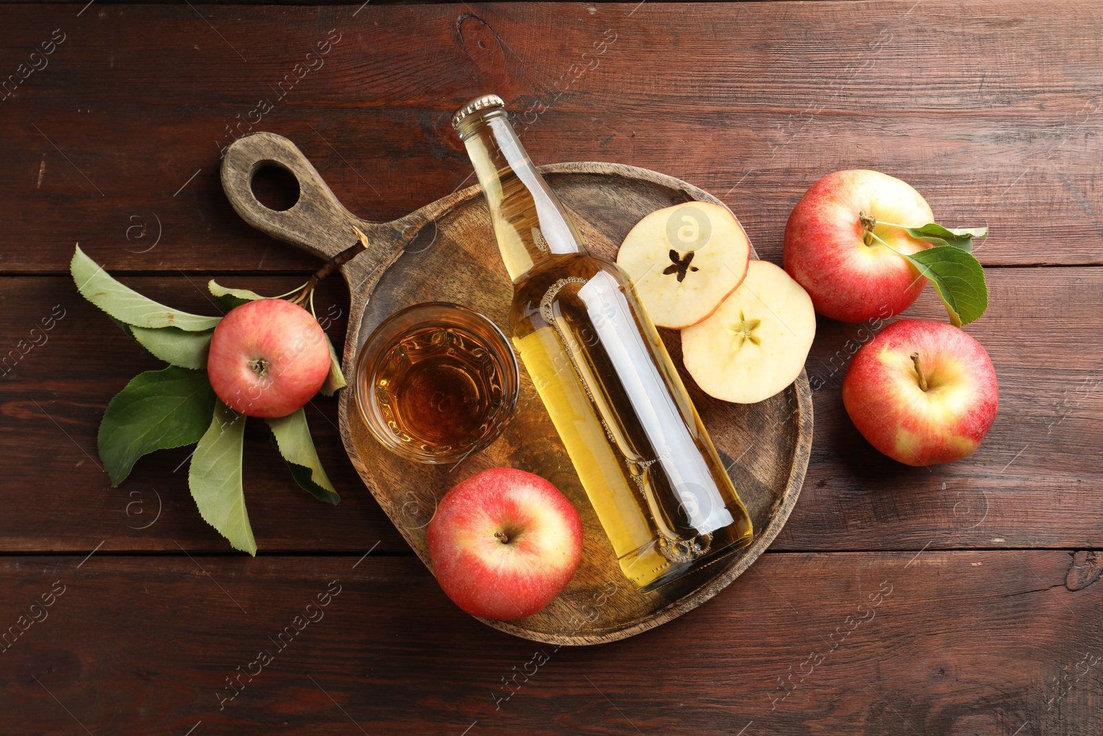 Photo of Delicious cider in bottle, glass and apples with green leaves on wooden table, flat lay