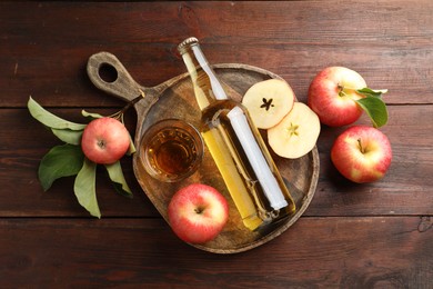 Photo of Delicious cider in bottle, glass and apples with green leaves on wooden table, flat lay