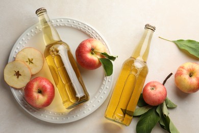 Photo of Delicious cider in glass bottles and apples with green leaves on beige table, flat lay