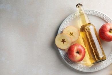 Photo of Delicious cider in glass bottle and apples on beige table, top view. Space for text