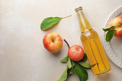 Photo of Delicious cider in glass bottle and apples with green leaves on beige table, flat lay. Space for text