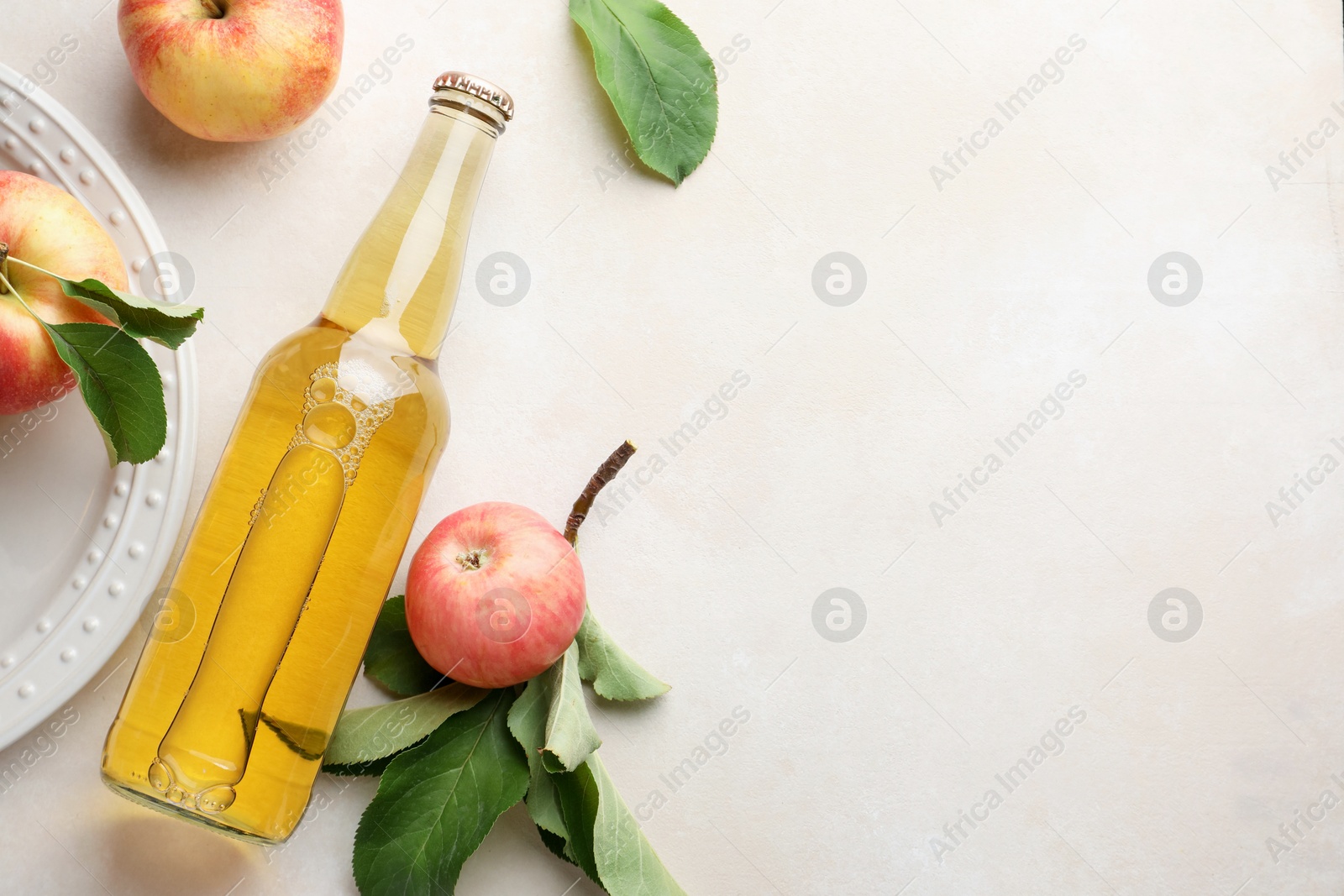 Photo of Delicious cider in glass bottle and apples with green leaves on beige table, flat lay. Space for text