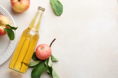 Photo of Delicious cider in glass bottle and apples with green leaves on beige table, flat lay. Space for text