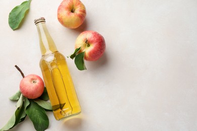 Photo of Delicious cider in glass bottle and apples with green leaves on beige table, flat lay. Space for text