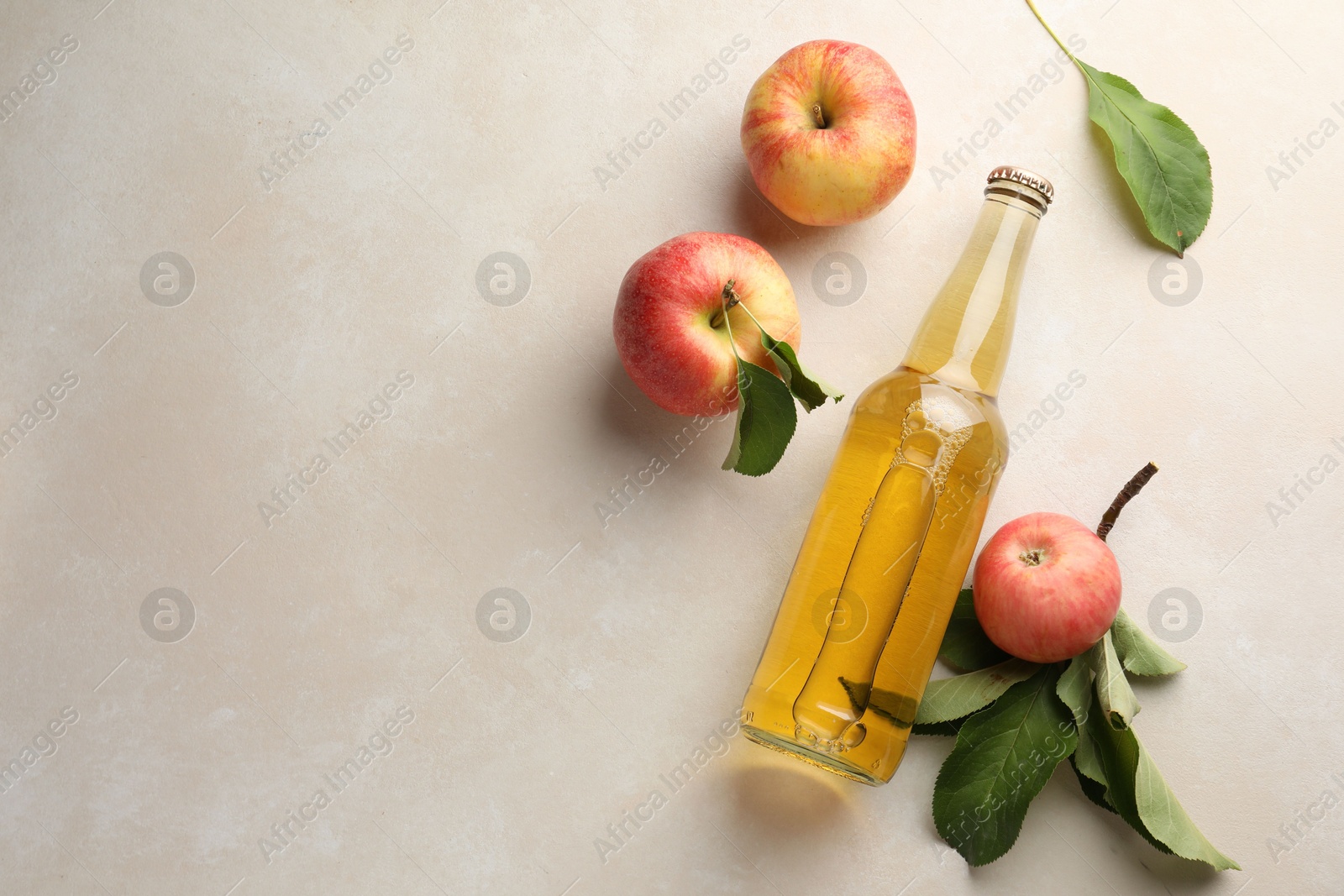 Photo of Delicious cider in glass bottle and apples with green leaves on beige table, flat lay. Space for text