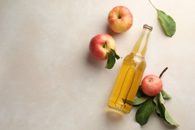 Photo of Delicious cider in glass bottle and apples with green leaves on beige table, flat lay. Space for text