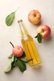 Photo of Delicious cider in glass bottle and apples with green leaves on beige table, flat lay