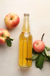 Photo of Delicious cider in glass bottle and apples with green leaves on beige table, flat lay