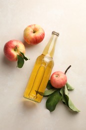 Photo of Delicious cider in glass bottle and apples with green leaves on beige table, flat lay