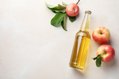 Photo of Delicious cider in glass bottle and apples with green leaves on beige table, flat lay. Space for text