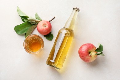 Photo of Delicious cider in bottle, glass and apples with green leaves on beige table, flat lay