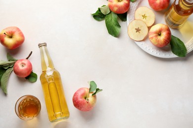 Photo of Delicious cider in bottles, glass and apples with green leaves on beige table, flat lay. Space for text